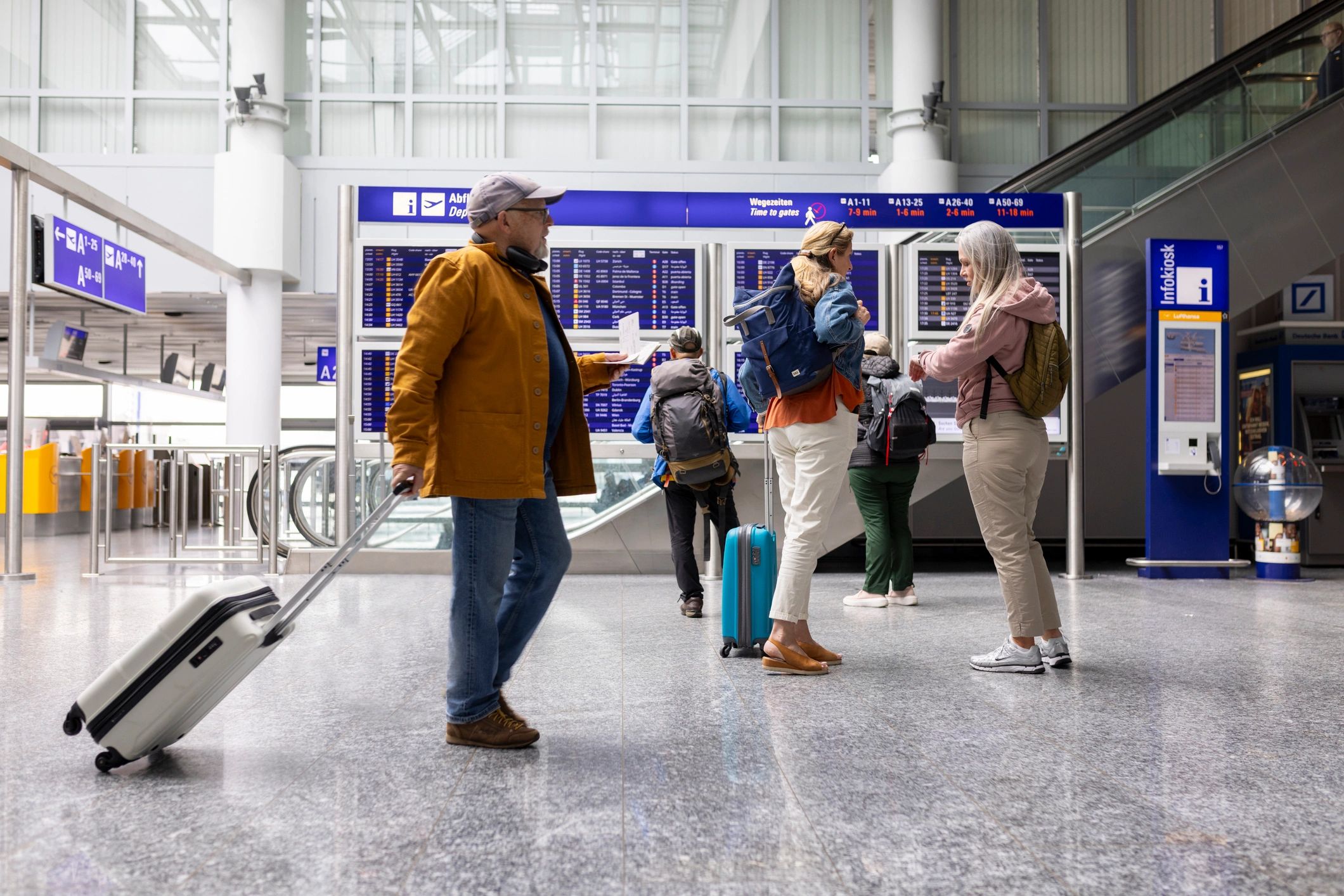 Travellers standing and walking around the airport in front of departure boards
