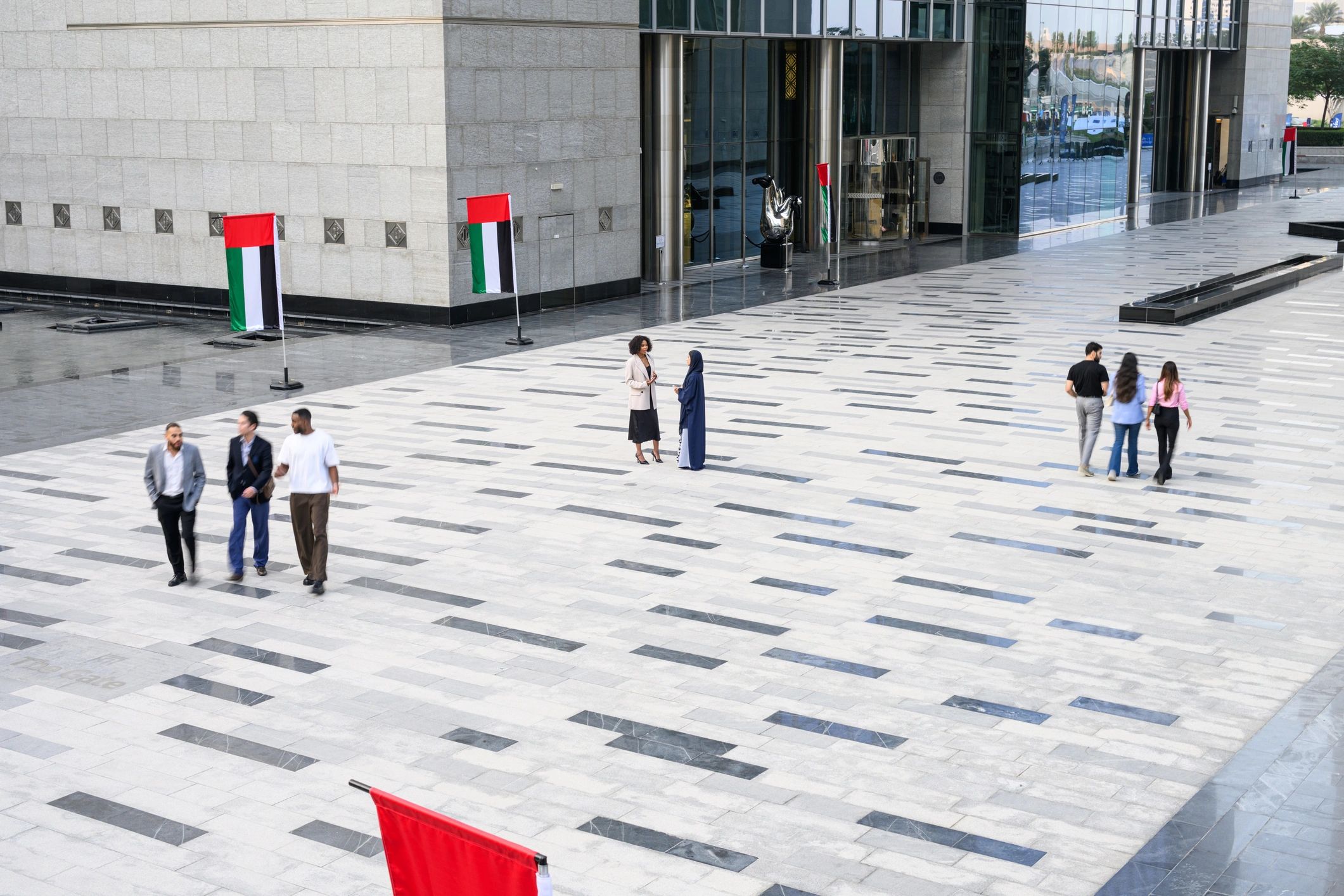 People walking in a modern Dubai business district plaza with UAE flags